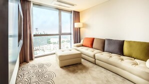 A modern hotel room with a large window, a beige sofa, an ottoman, and a patterned rug. - Hotel Golden Daisy Seogwipo Ocean (Seogwipo)