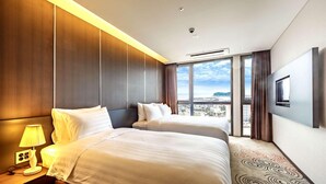 A hotel room with two beds, a large window with a city view, a flat-screen TV mounted on the wall, and a patterned carpet. - Hotel Golden Daisy Seogwipo Ocean (Seogwipo)