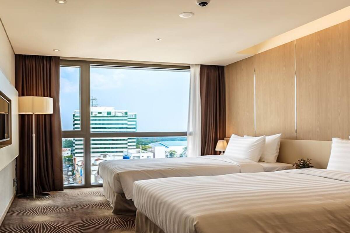 A hotel room with two beds, a large window with a city view, and a modern design.