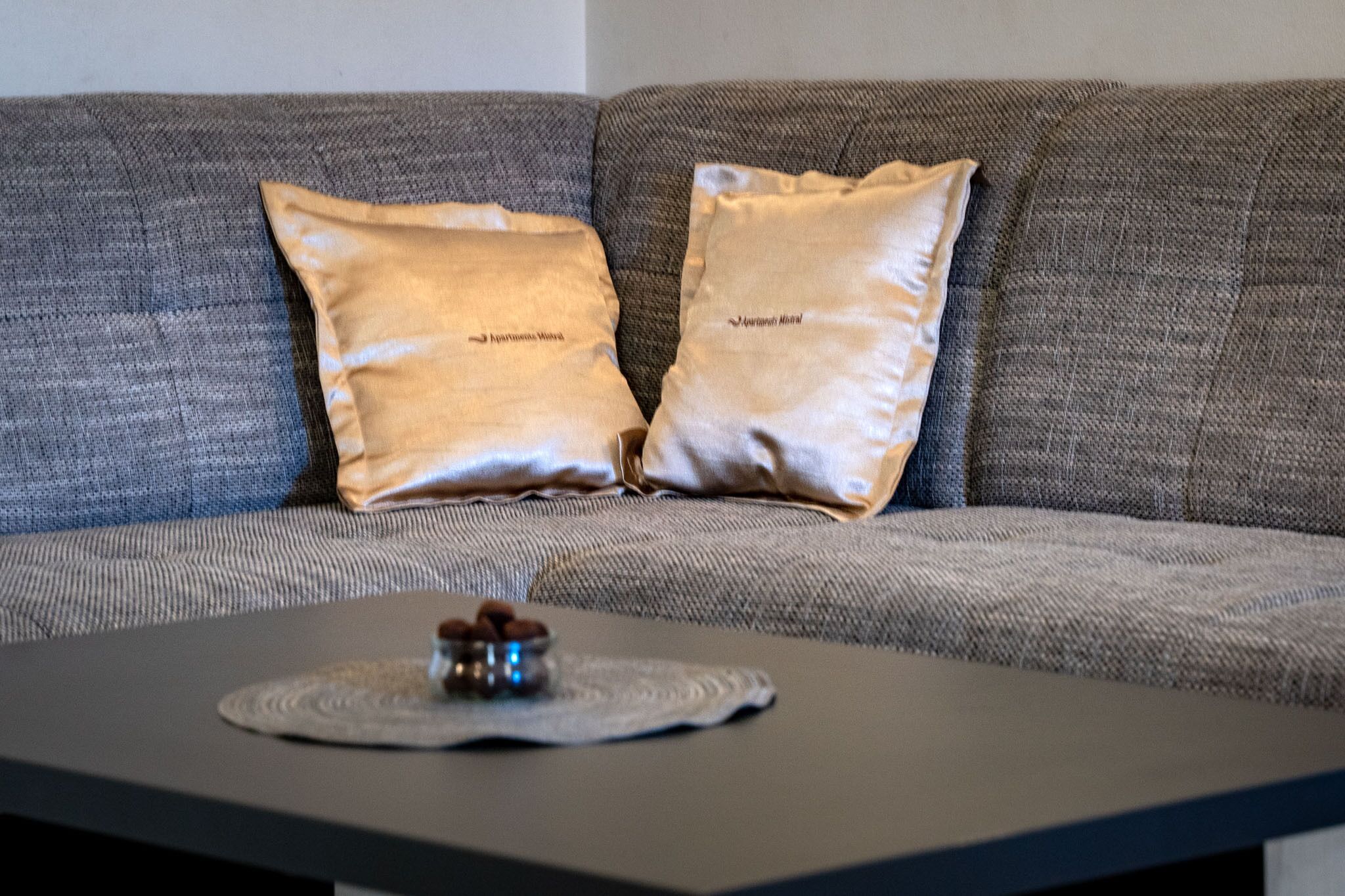 A grey sofa with two pillows and a small table with a decorative item.
