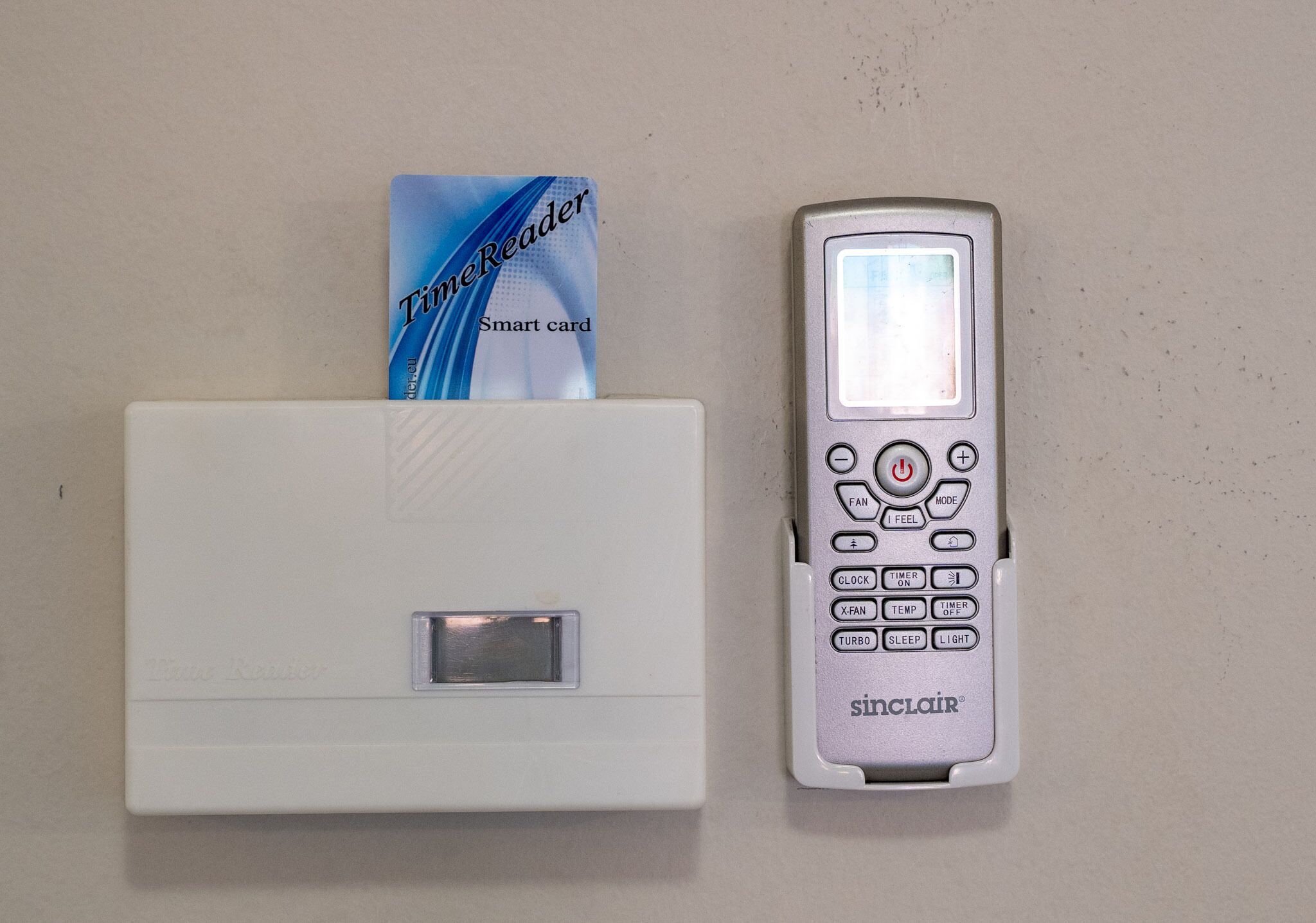 A white bedside table with a card slot and a silver bedside clock with multiple buttons.