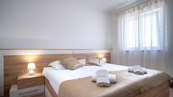 A neatly made bed with a wooden headboard, two bedside lamps, and a window with sheer curtains.