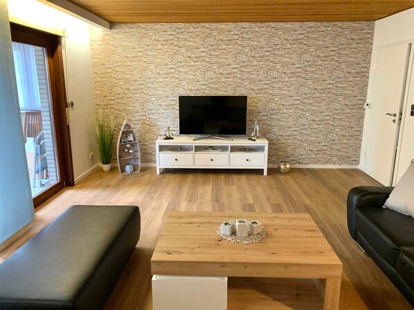 A living room with a stone wall, a TV, a white cabinet, a wooden coffee table, and a black sofa.