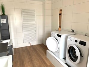 A modern laundry room with two washing machines, a radiator, and a wooden floor.