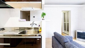 A modern kitchen with a stainless steel sink and a dining area with a grey sofa. - Eve (Sapporo)