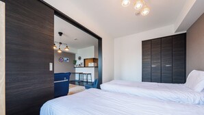 Ett modernt hotellrum med två sängar, en mörk trägarderob och en matplats som syns genom en öppen dörr.