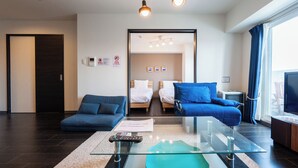 Ett modernt hotellrum med ett soffbord i glas, en soffa, en säng med blått sänglinne och en tv.