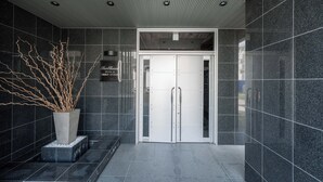 En modern entréhall med ett mörkt klinkergolv, en stor krukväxt och en dubbeldörr.