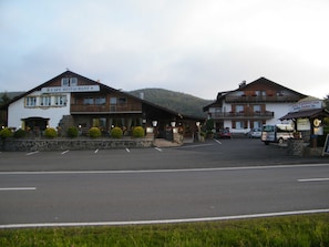 Ein zweistöckiges Gebäude mit Café und Restaurant im Erdgeschoss, einem Parkplatz davor und einem Berg im Hintergrund.