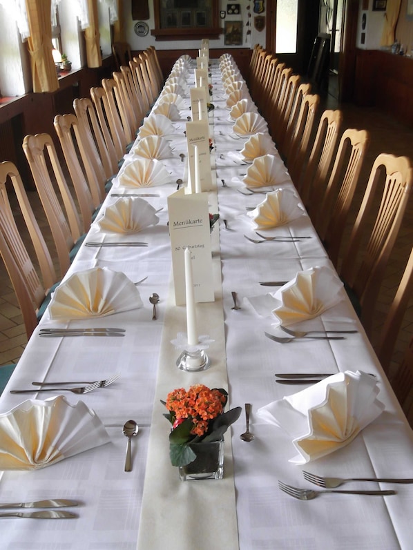 A long dining table set with white tablecloths, folded napkins, and silverware.
