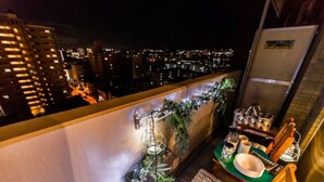 Un balcón con comedor, que incluye una mesa con platos y cubiertos, y una vista nocturna de la ciudad.