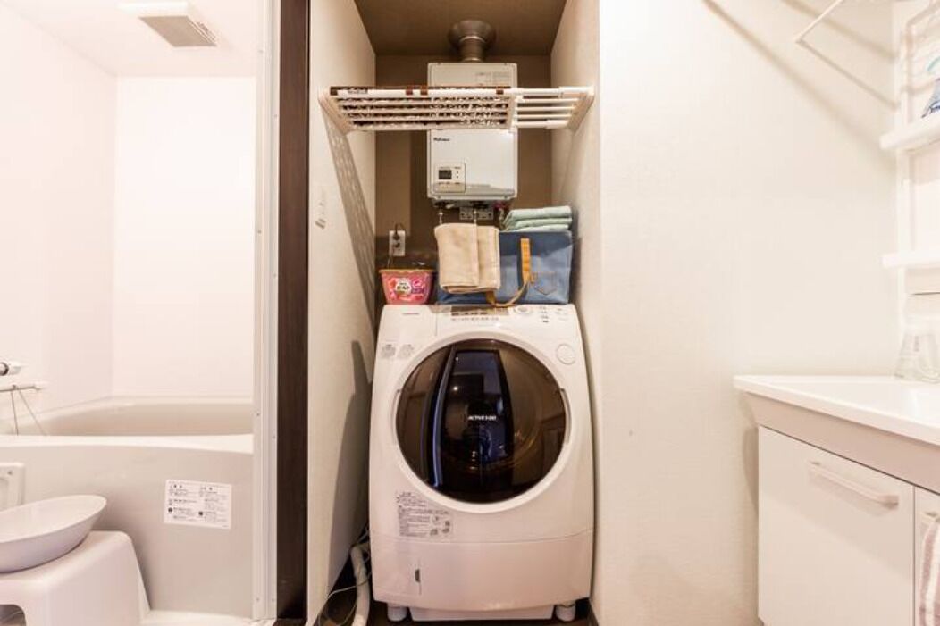 A compact laundry room with a front-loading washing machine, a dryer, and a small shelf with folded clothes and a basket.