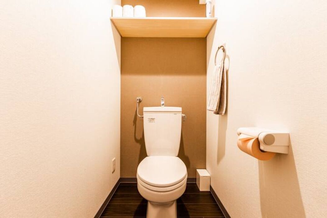 A small, compact bathroom with a toilet, a shelf with toiletries, and a towel rack.