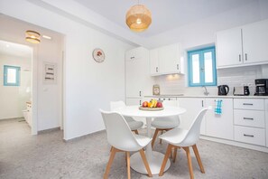 A modern kitchen with white cabinets, a round dining table with four chairs, and a fruit bowl on the table.