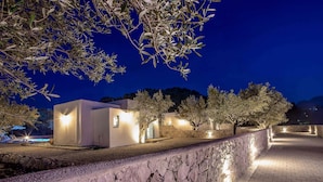 Un muro di pietra, un vialetto lastricato e un edificio con finestre illuminate di notte.