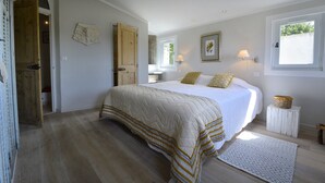 A bedroom with a large bed, wooden flooring, a small bedside table, a window with a view, and a door leading to another room. - Séguret, cosy village house with exceptional view (Seguret)