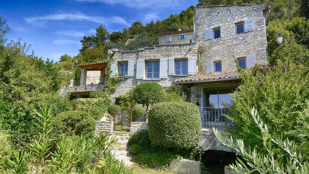 A stone building with multiple windows and a balcony, surrounded by lush greenery and trees. - Séguret, cosy village house with exceptional view (Seguret)