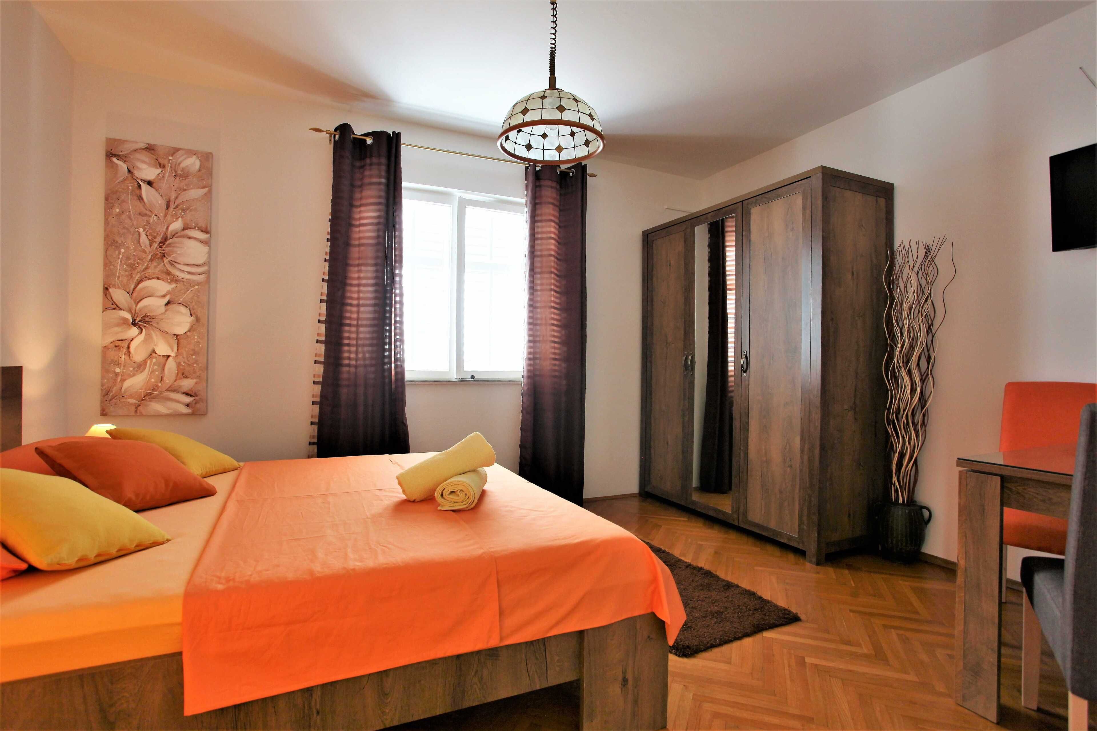 A bedroom with a bed, a wardrobe, a chair, and a hanging light fixture.