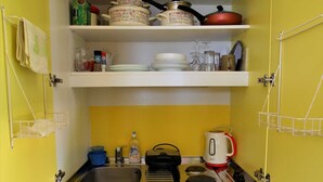 Uma cozinha compacta com armários amarelos, uma pia, uma chaleira e diversos utensílios de cozinha.