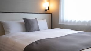 Cama bem arrumada com roupa de cama branca e cinza, cabeceira e luminária fixa na parede.