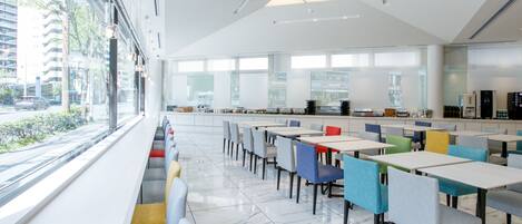 A modern cafeteria with white marble floors, colorful chairs, and a large window overlooking a cityscape.