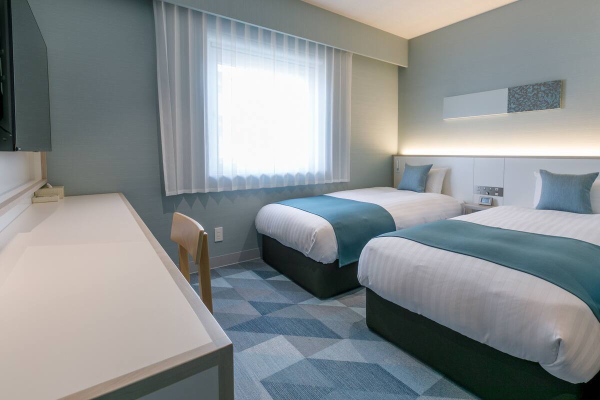 Une chambre d’hôtel avec deux lits, un bureau et une chaise.