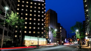 Um hotel moderno com uma placa em japonês, vários andares e fachada bem iluminada.