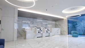Uma área de recepção moderna, com piso de mármore, balcão de atendimento e uma cadeira azul.