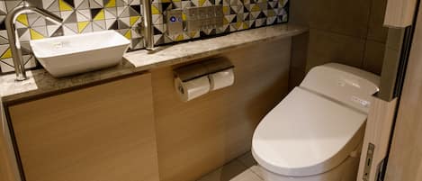 A modern bathroom with a white toilet, a sink with a mirror above it, and a patterned tile backsplash.