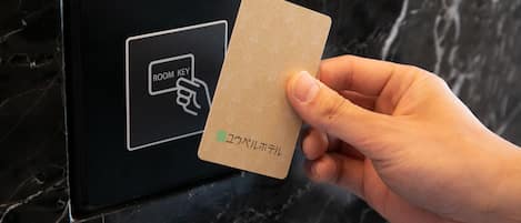 A hand holding a card with a room key icon and Japanese text, next to a black box with a similar icon.