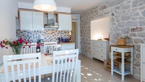 Una cocina compacta con armarios blancos, salpicadero de azulejos y pared de piedra.