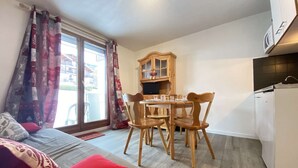 A cozy room with a bed, a dining table with chairs, a wooden cabinet, and a refrigerator. - Cozy Garden-Level Studio Cabin in Praz-sur-Arly - Sleeps 4 (Praz-sur-Arly)