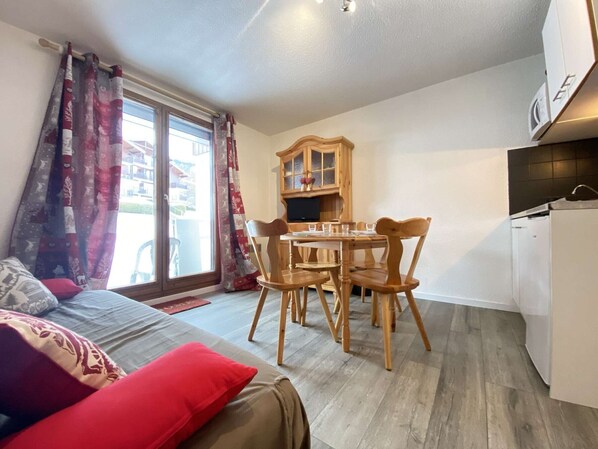 A cozy room with a bed, a dining table with chairs, a wooden cabinet, and a refrigerator. - Cozy Garden-Level Studio Cabin in Praz-sur-Arly - Sleeps 4 (Praz-sur-Arly)