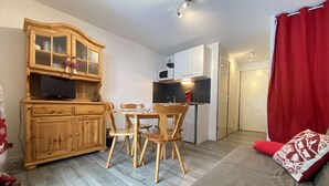 A compact living space with a dining area, kitchenette, and a sofa with red cushions. - Cozy Garden-Level Studio Cabin in Praz-sur-Arly - Sleeps 4 (Praz-sur-Arly)