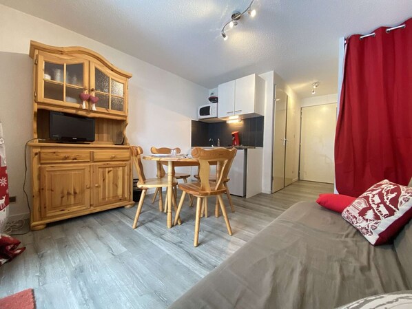 Un espacio habitable compacto con comedor, kitchenette y un sofá con cojines rojos.