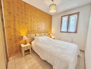 Ein Schlafzimmer mit Holzwand, einem Bett mit weißer Bettwäsche, zwei Nachttischen mit Lampen und einem Fenster mit Vorhängen.