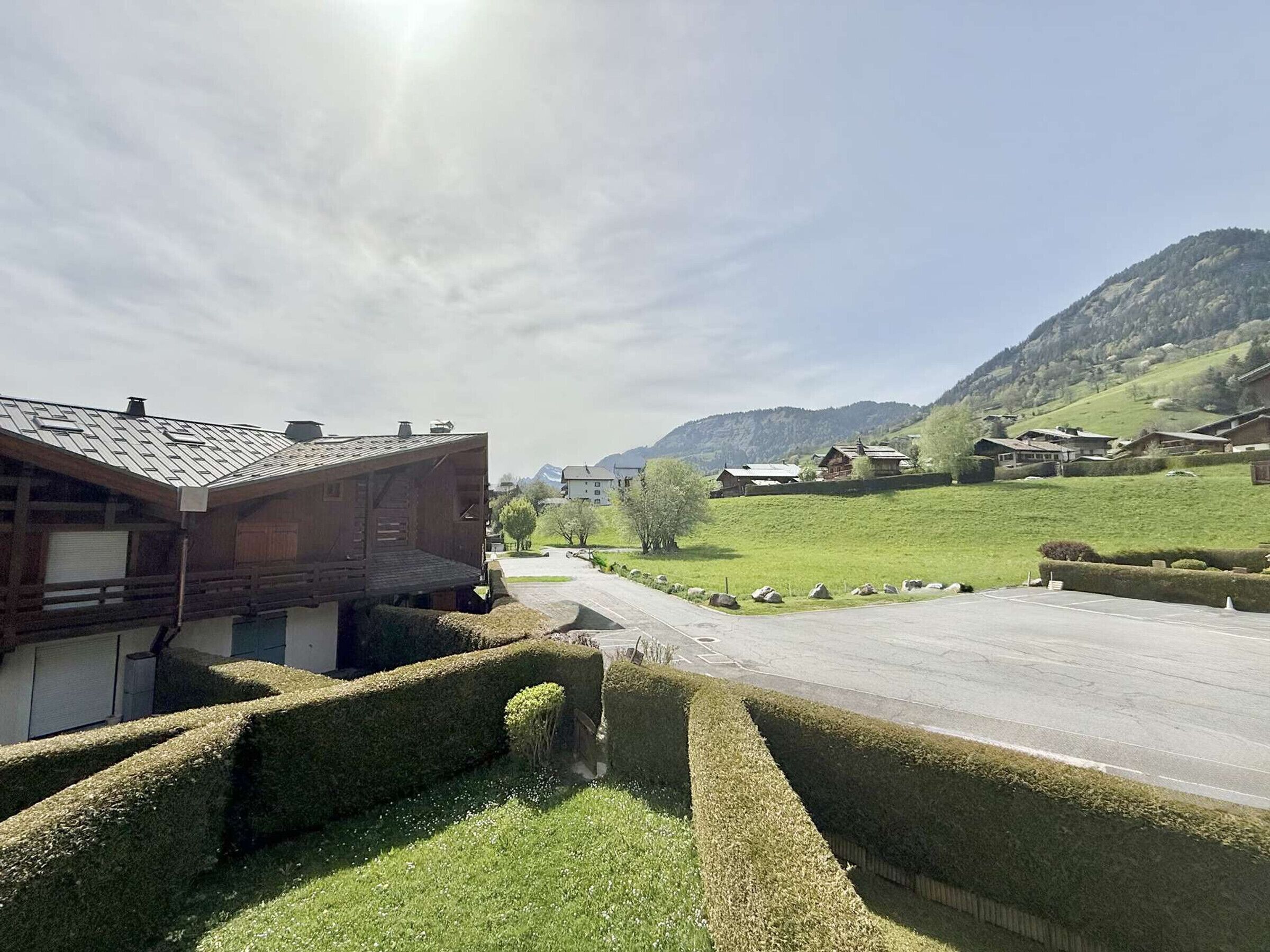 Un paysage rural avec un bâtiment en bois, une route asphaltée et des collines verdoyantes en arrière-plan.