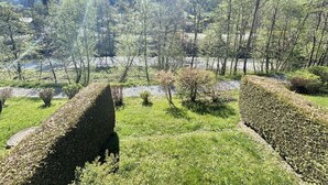 En anlagt have med velplejede hække, en klar himmel og et bjerglandskab i baggrunden.