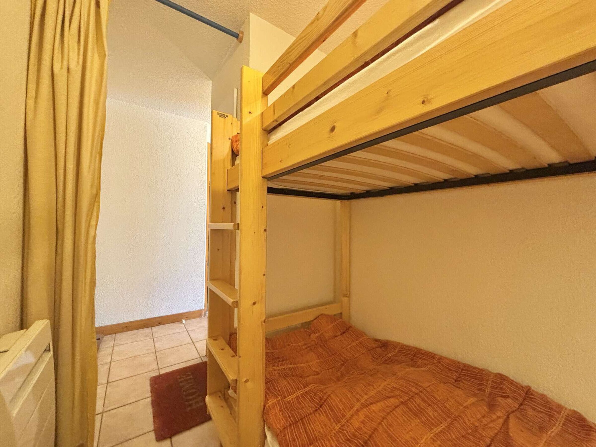 Una habitación pequeña con una cama individual tipo litera de madera, una puerta y suelo de baldosas.