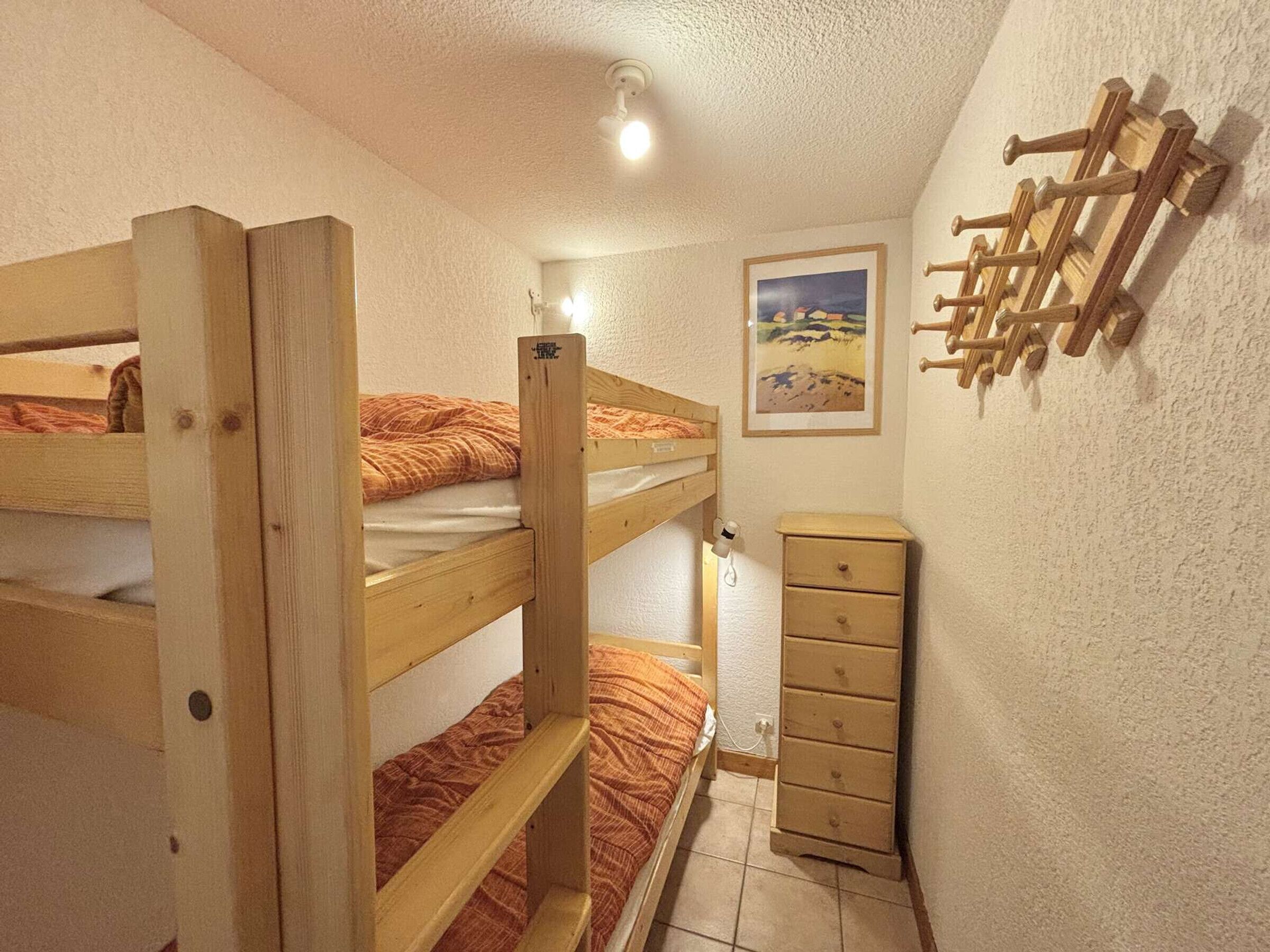 A bunk bed room with a wooden dresser and a wall-mounted rack.