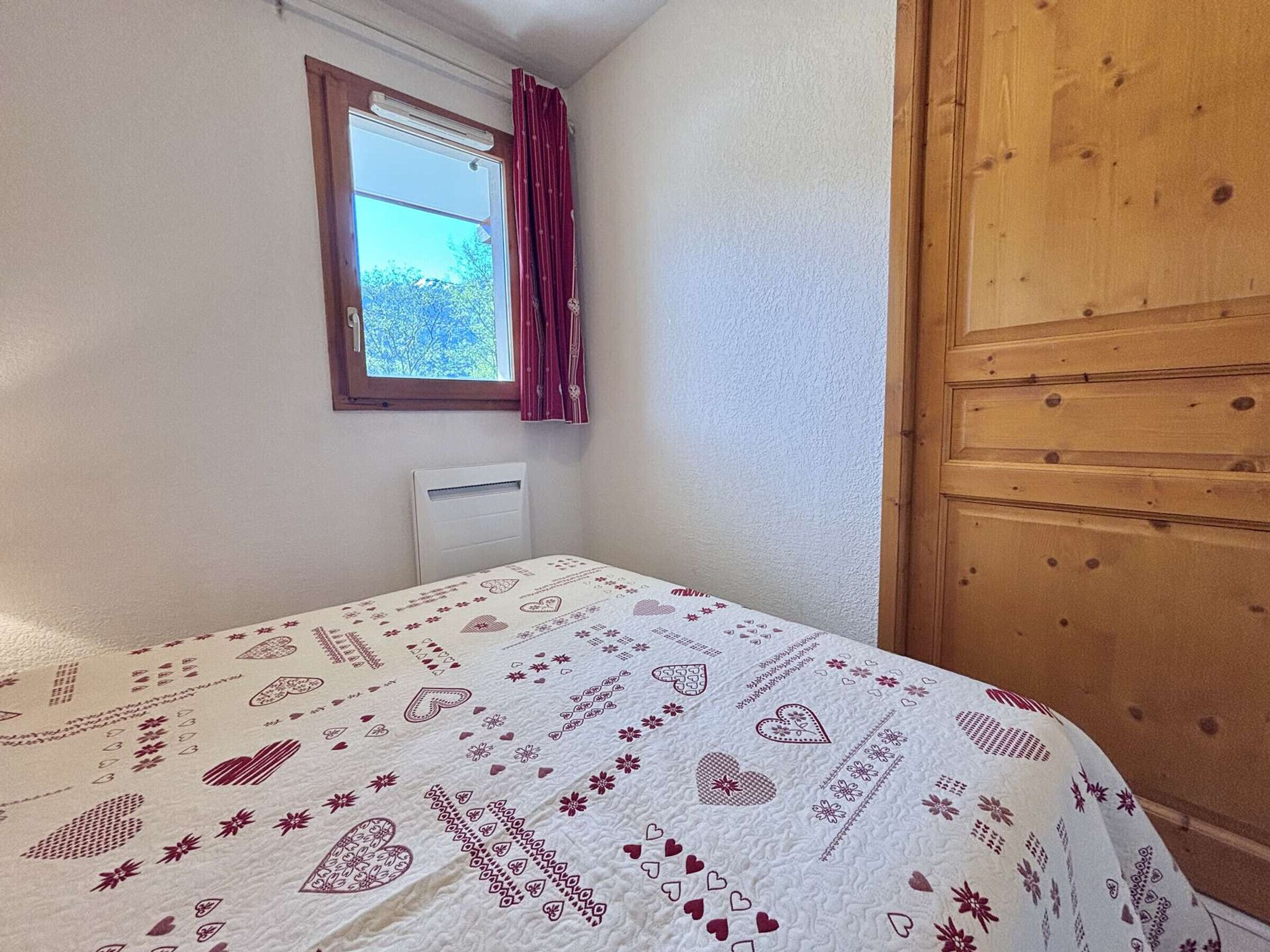 A bedroom with a bed, a window with curtains, a radiator, and a wooden door.