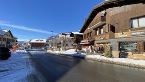 A snow-covered street with wooden buildings, including a ski shop and a restaurant. - Studio cabin, pets welcome - 4 guests, views of ski slopes (Praz-sur-Arly)