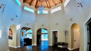A spacious hall with a high wooden ceiling, large windows, and a chandelier.