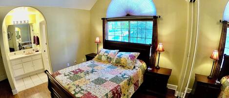 Une chambre avec un grand lit, une coiffeuse avec un miroir et une fenêtre donnant sur les arbres.