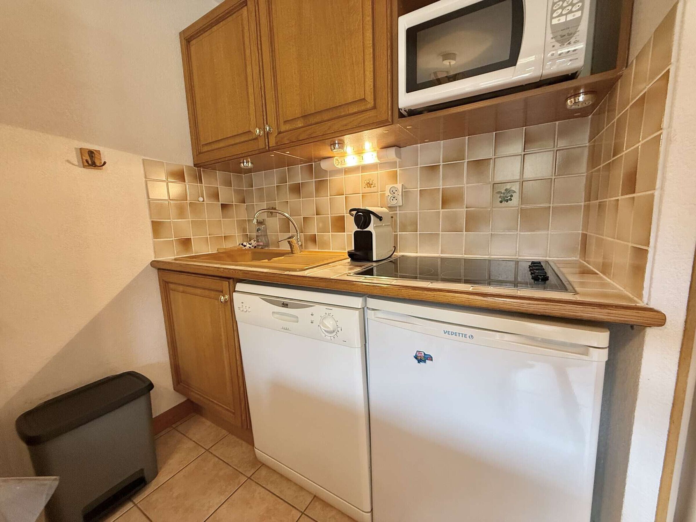 A compact kitchen with wooden cabinets, a microwave, a sink, and a dishwasher.