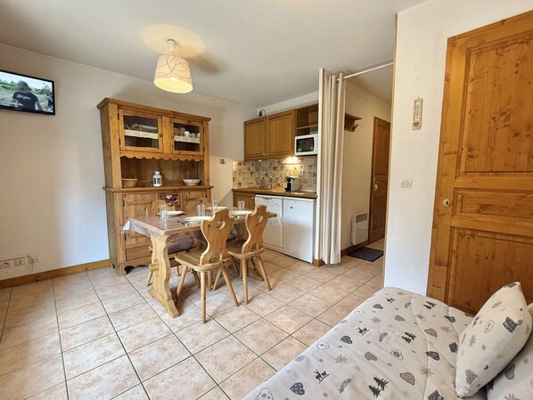 A compact kitchen with wooden cabinets, a dining table, and chairs. There is a microwave and a small refrigerator.