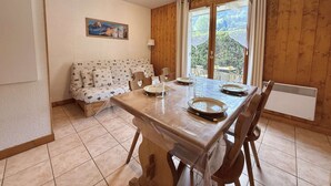 A dining area with a wooden table set for four, a sofa with a patterned cover, and a painting on the wall.
