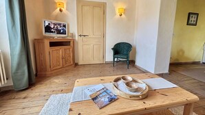 A cozy room with a wooden floor, a television on a cabinet, a green chair, and a table with a magazine and a tray with cups. - Cozy apartment in Praz-sur-Arly, 2 rooms, near village (Praz-sur-Arly)