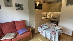 Um espaço de estar compacto com uma mesa de jantar de madeira para quatro pessoas, um sofá vermelho com almofadas e um pequeno banquinho de madeira.
