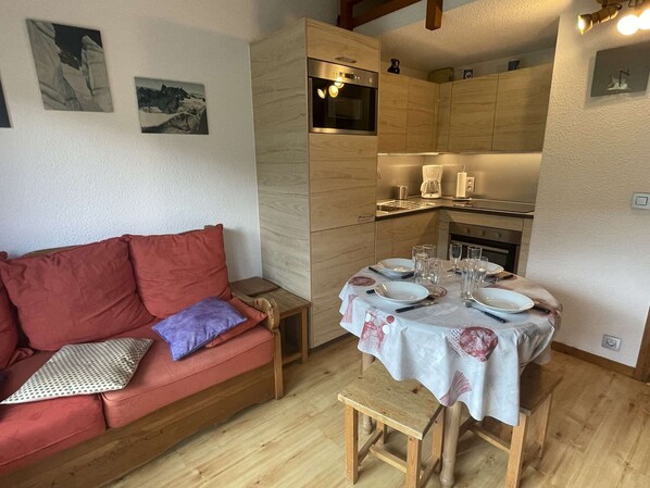 Un espace de vie compact comprenant une table de salle à manger en bois pour quatre personnes, un canapé rouge avec des coussins et un petit tabouret en bois.